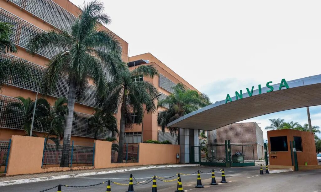 Fachada externa do prédio da ANVISA, com palmeiras e entrada principal visível.