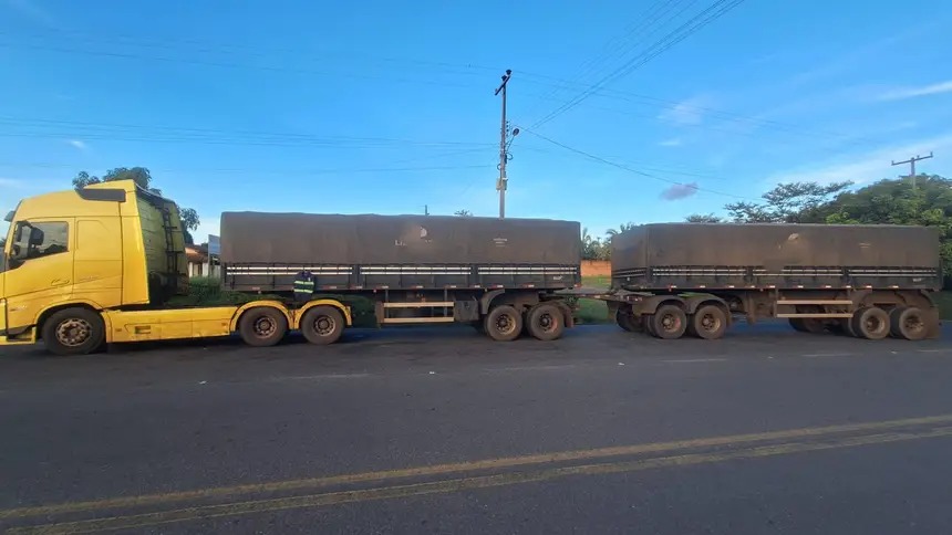 Caminhão amarelo Volvo com dois reboques cobertos em estrada.