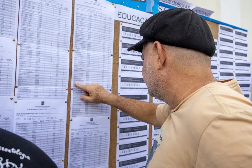 Homem de boné examinando uma lista em mural de educação.