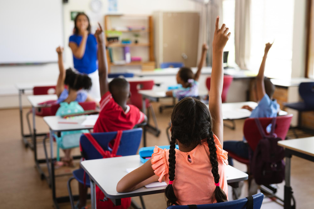 Crianças em sala de aula levantando as mãos para responder perguntas.