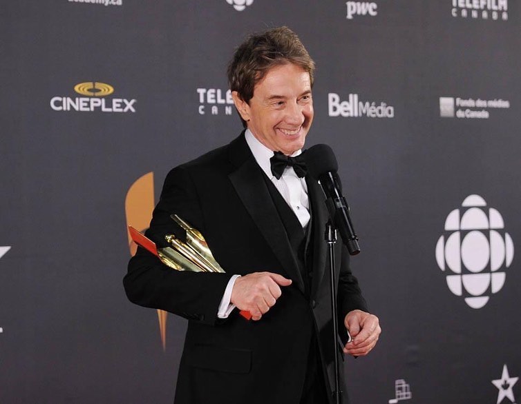 Martin Short sorrindo e segurando um troféu dourado em evento de gala.