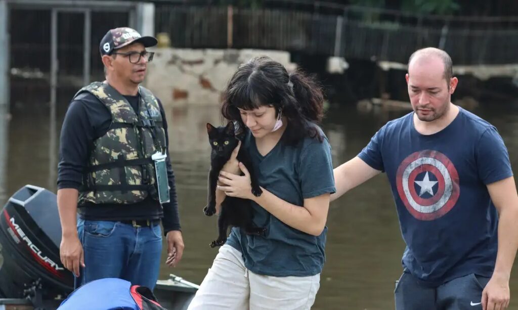 Mulher segurando um gato preto resgatado em meio a uma enchente, com voluntários por perto.