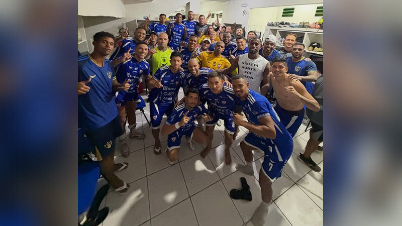 Grupo de jogadores de futebol em um vestiário, celebrando uma vitória.