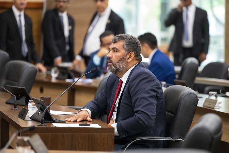 Homem barbudo de terno em mesa de reunião com microfone.