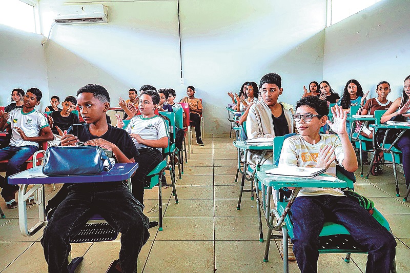 Alunos em sala de aula levantando as mãos e aplaudindo durante uma atividade educativa.