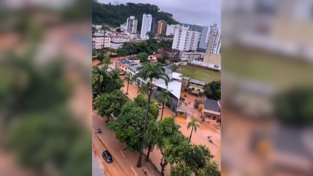 Enchente em rua de cidade com carros submersos e prédios ao fundo.