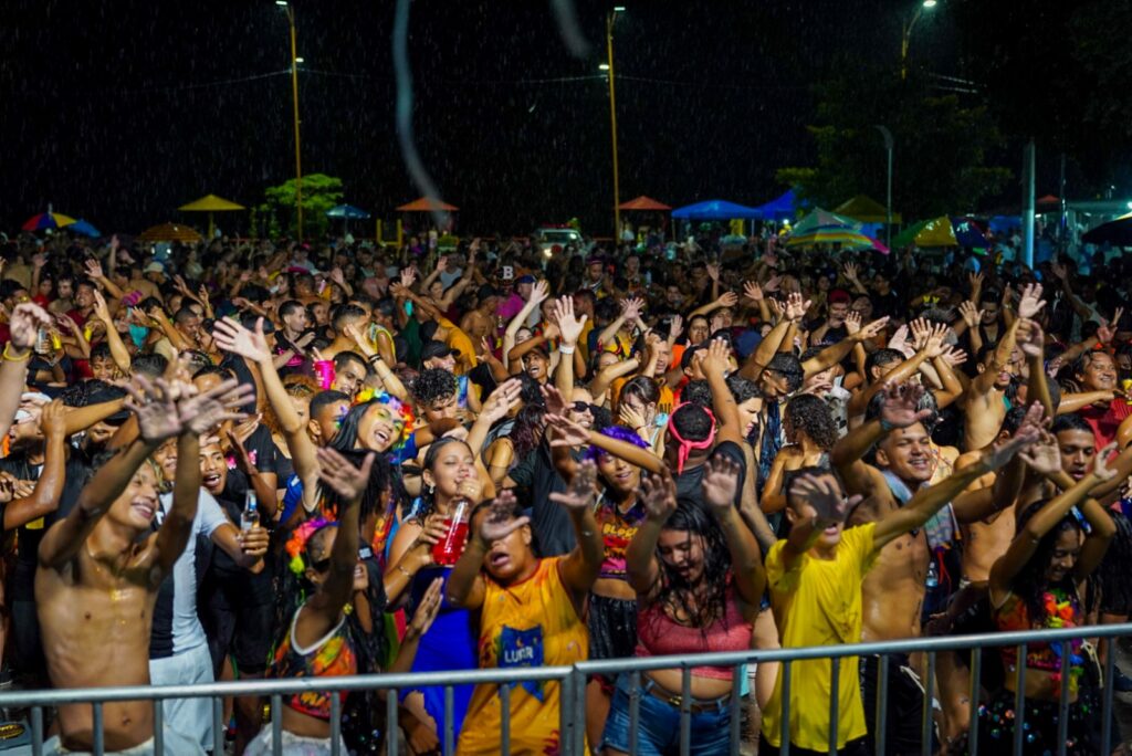 Multidão animada em evento noturno com mãos para o alto, festejando ao ar livre.