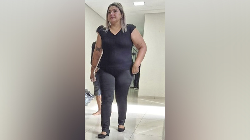 Mulher de blusa preta e calça preta em pé em um corredor.