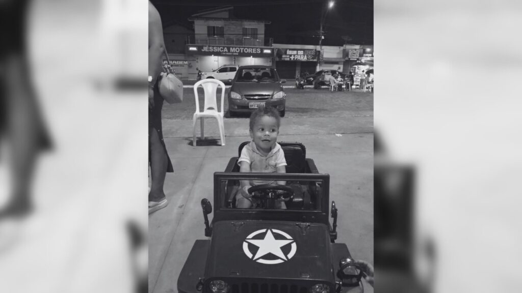 Foto em preto e branco de um bebê sorridente em um jipe de brinquedo com estrela.