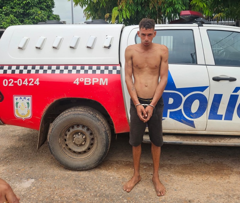 Homem algemado em pé na frente de uma viatura policial.