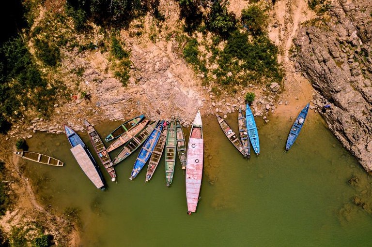 Vista aérea de barcos tradicionais coloridos ancorados em margem rochosa de rio.