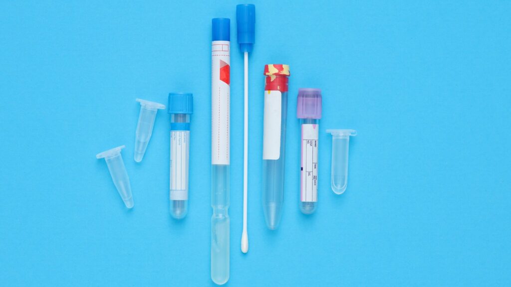 Tubos de ensaio e swab para coleta de amostras em fundo azul.
