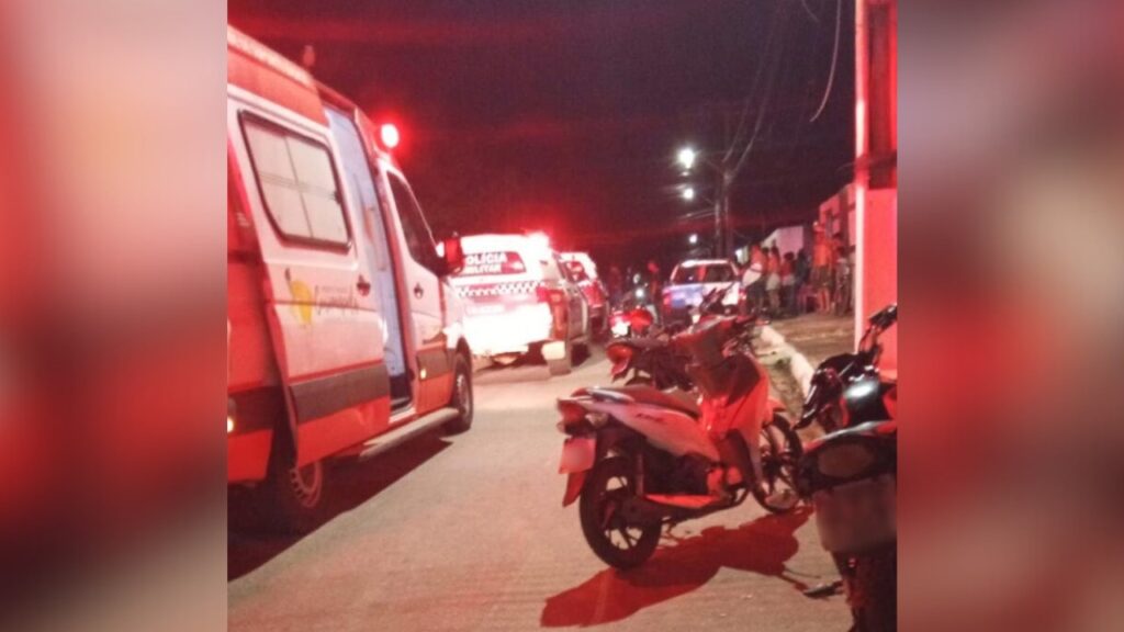 Ambulância e viatura policial com luzes de emergência acesas em rua à noite.