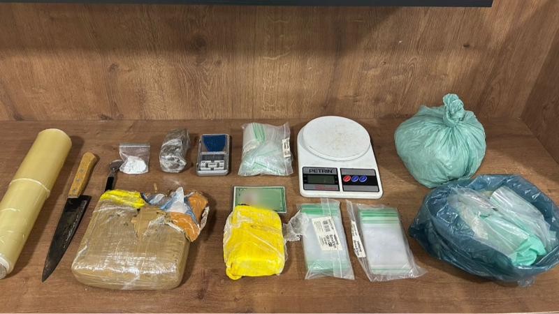 Objetos apreendidos em operação policial: drogas, balanças de precisão e facas sobre mesa de madeira.