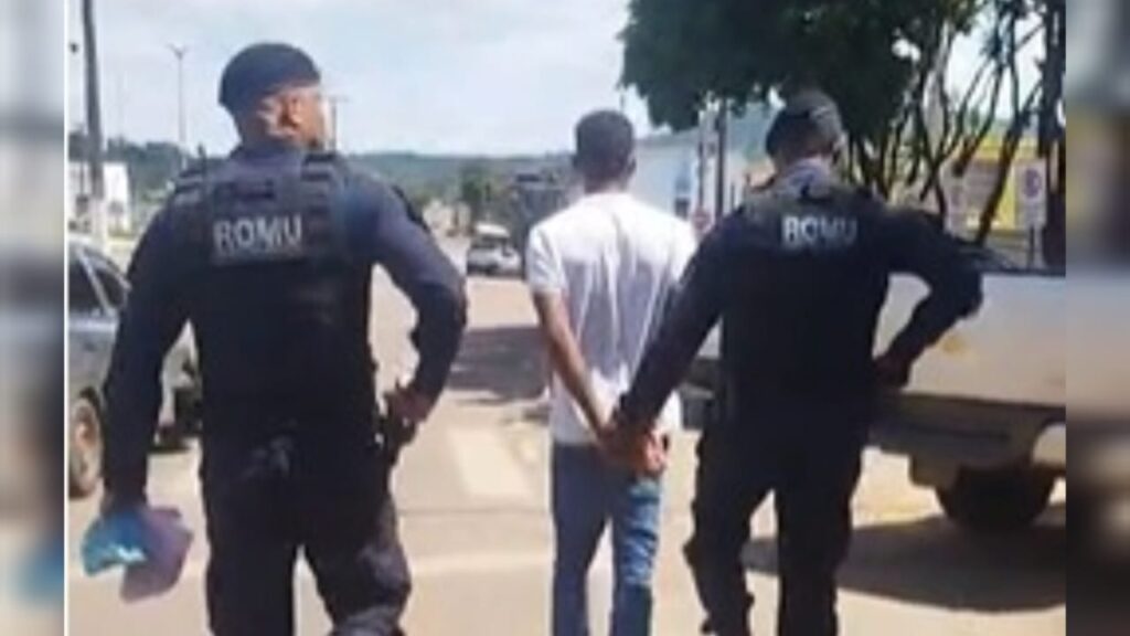Pessoa algemada sendo escoltada por dois guardas municipais da ROMU em uma rua.