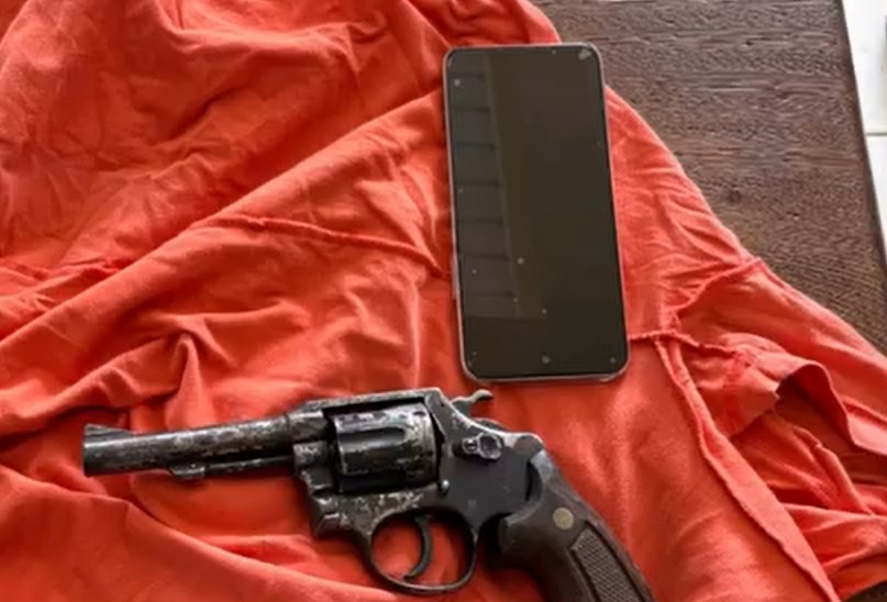 Revólver e smartphone sobre tecido laranja amarrotado.