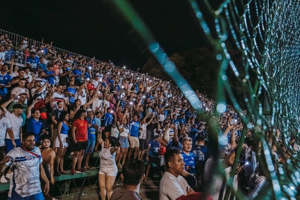 Multidão em estádio à noite com celulares acesos na arquibancada.