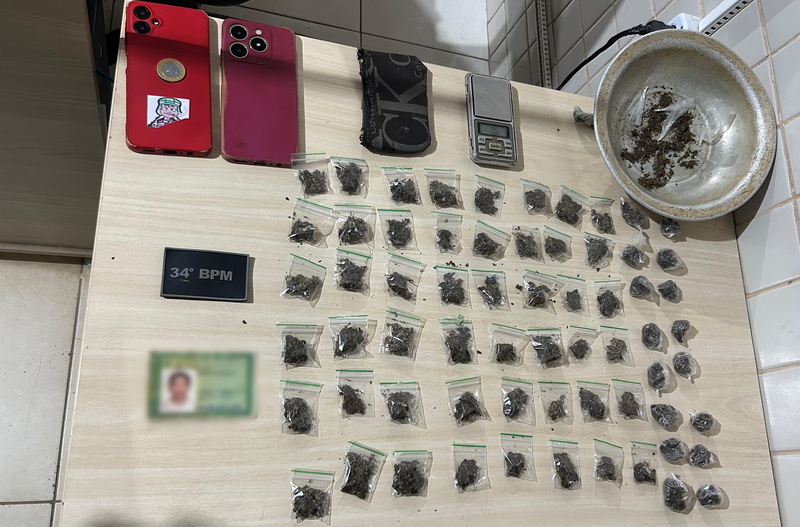 Mesa com diversos sacos plásticos contendo substância vegetal, dois celulares, balança de precisão e placa '34° BPM'.