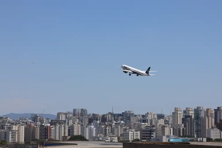 Avião da Azul decolando sobre paisagem urbana em dia claro.