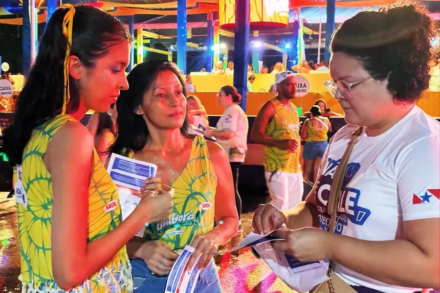 Duas mulheres em evento festivo noturno com glitter, segurando panfletos.