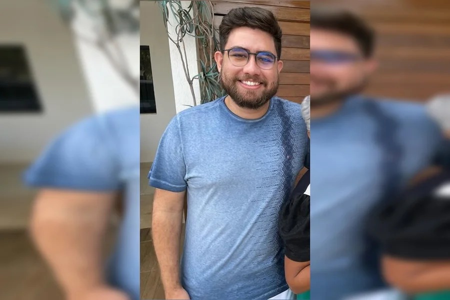 Homem barbudo de óculos e camiseta azul sorrindo para a câmera.