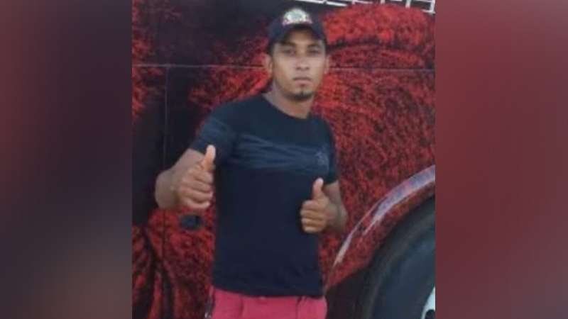 Jovem com boné e camiseta escura fazendo sinal de "joinha" com as duas mãos.