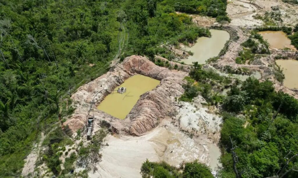 Vista aérea de garimpo ilegal com cavas de água barrenta e máquinas em meio à floresta amazônica.
