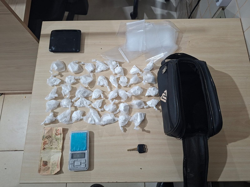 Apreensão de drogas, balança de precisão, dinheiro e chave em uma mesa de madeira.