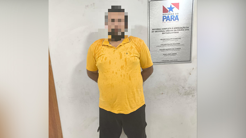 Homem com rosto pixelado e camisa polo amarela, em pé diante de parede branca e placa do Governo do Pará.
