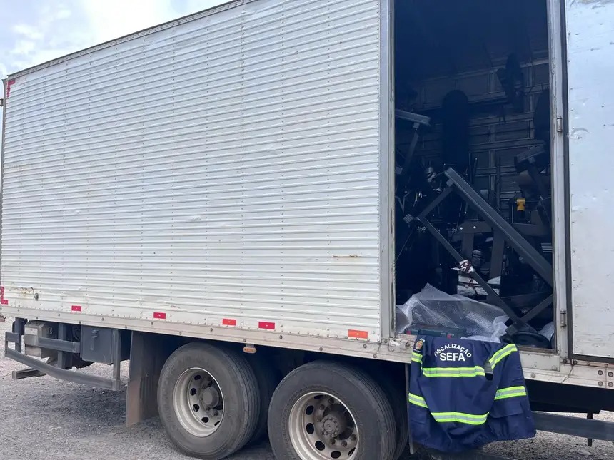 Caminhão baú branco com porta traseira aberta e jaqueta 'FISCALIZAÇÃO SEFA' pendurada.