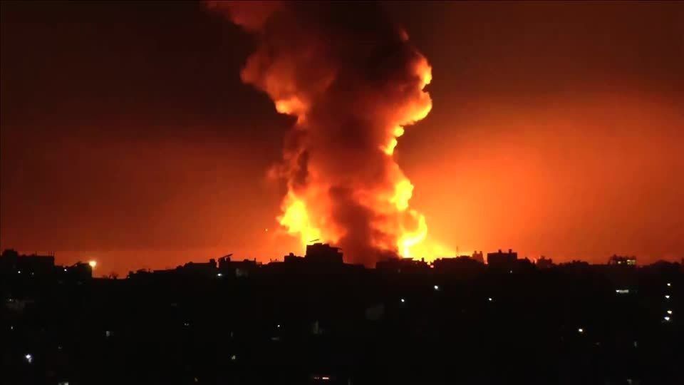Explosão massiva com chamas e fumaça em uma cidade à noite.