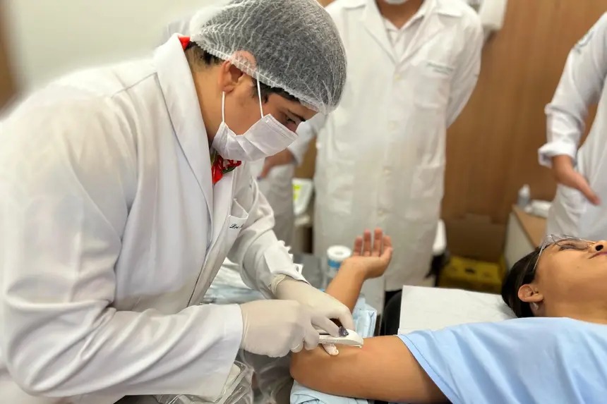 Profissional de saúde com jaleco e máscara coletando amostra do braço de um paciente.