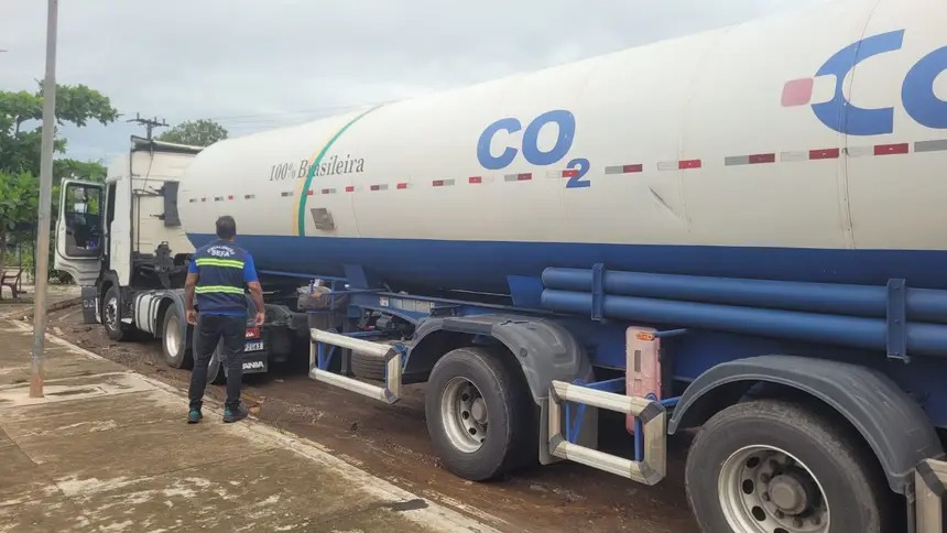 Caminhão-tanque branco e azul com inscrição "CO2" e "100% Brasileira" em terreno enlameado.
