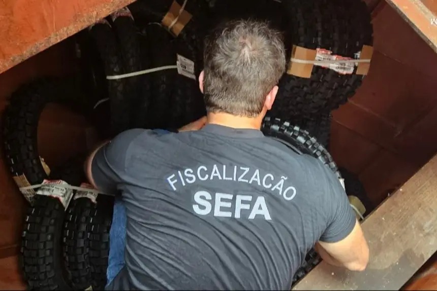 Homem com camiseta "FISCALIZAÇÃO SEFA" inspecionando pneus.