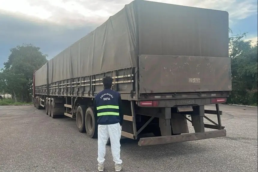 Fiscal da SEFA de costas inspecionando a traseira de um caminhão-reboque em estrada.