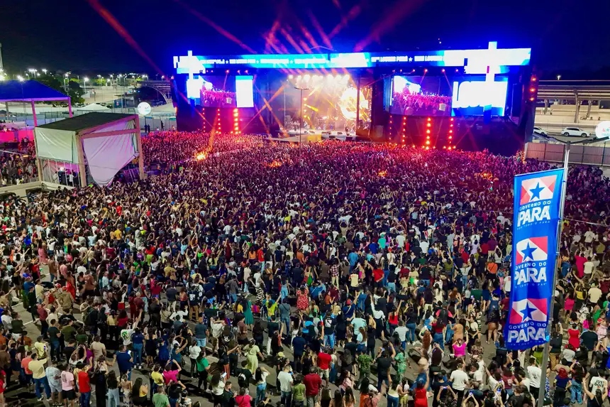 Multidão em show noturno com palco iluminado e telões.
