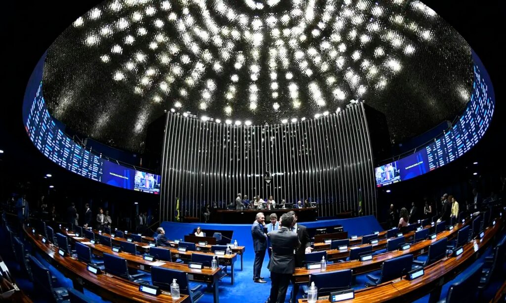 Interior do Plenário do Senado Federal com teto abobadado iluminado e parlamentares em interação.