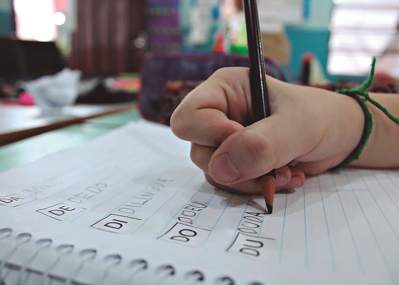 Foco na mão de uma criança escrevendo com lápis em um caderno de caligrafia.