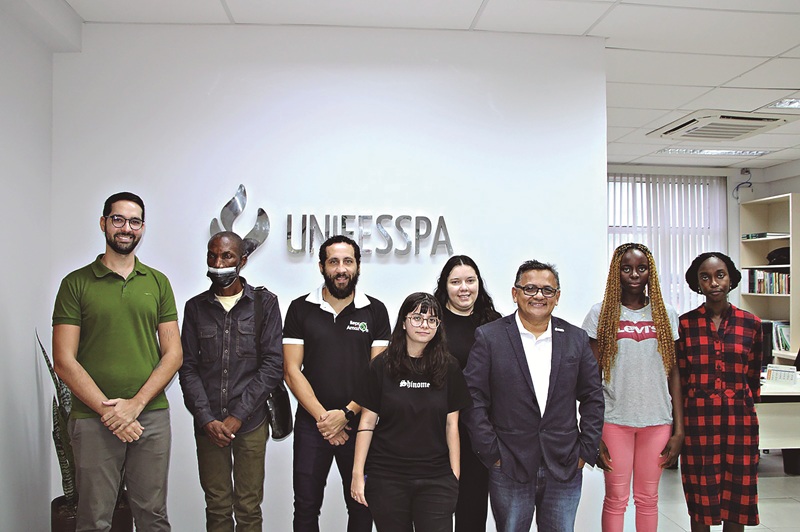 Grupo diverso de 9 pessoas sorrindo em frente ao logo da UNIFESSPA.