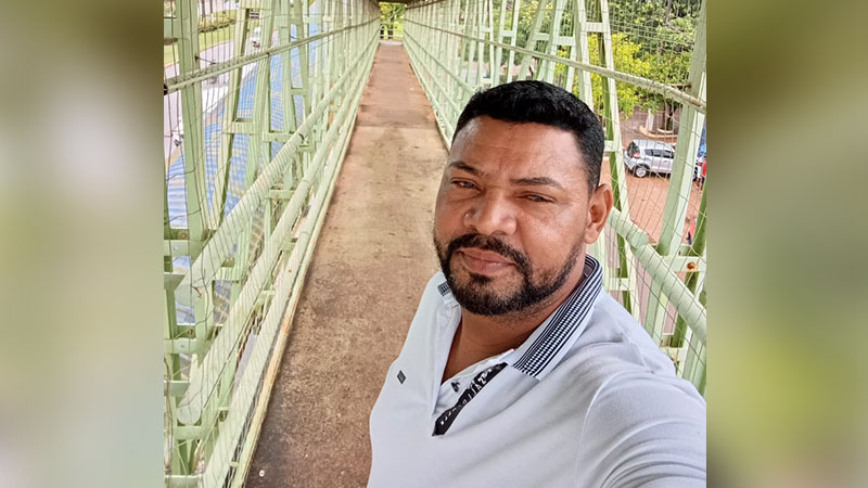 Homem barbudo de camisa branca sorrindo em passarela verde.