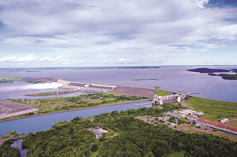 Vista aérea de uma usina hidrelétrica em funcionamento, com água jorrando.