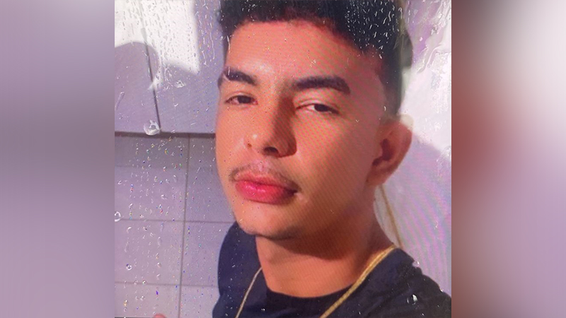 Retrato de um jovem com bigode e corrente dourada, olhando para a câmera.