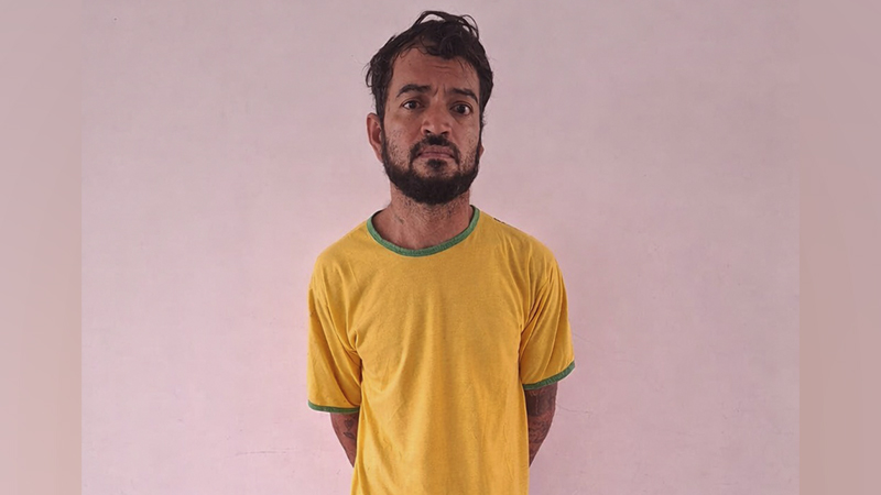 Homem barbudo com camiseta amarela e detalhes verdes em fundo rosa.