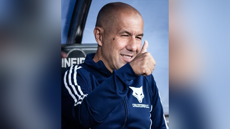 Homem careca sorrindo e fazendo sinal de positivo, vestindo agasalho do Cruzeiro E.C.