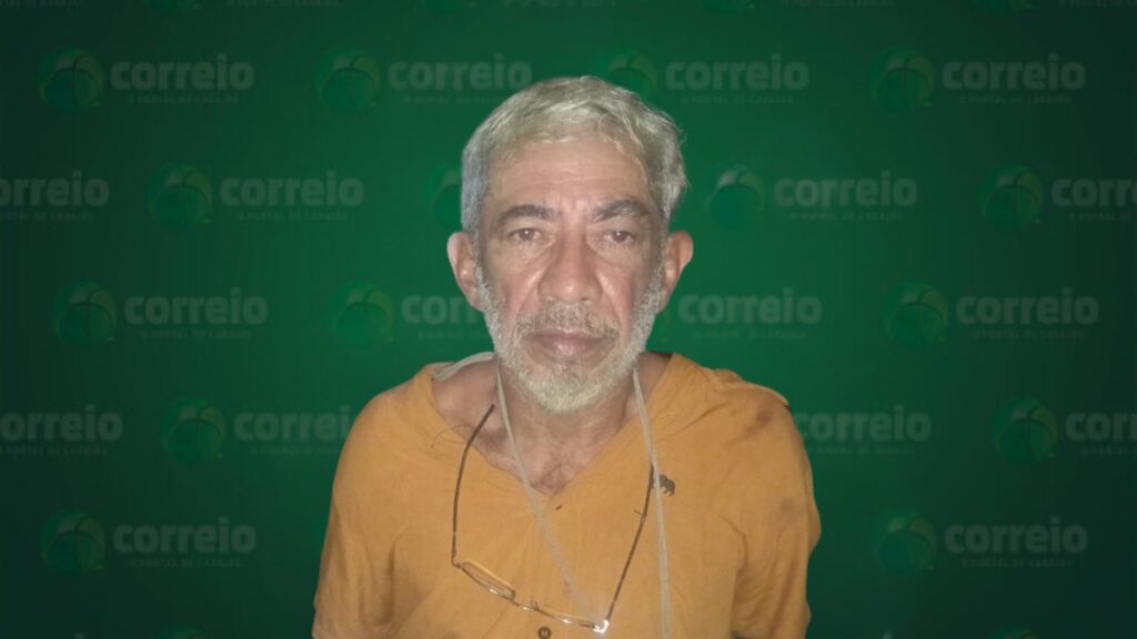 Homem com cabelo e barba grisalhos, óculos no pescoço, em frente a fundo verde com logo "correio".