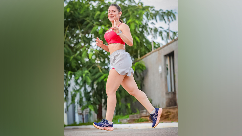 Mulher sorridente correndo em trajes esportivos ao ar livre.