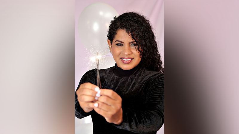Mulher sorrindo segurando um sparkler aceso com um balão branco ao fundo.