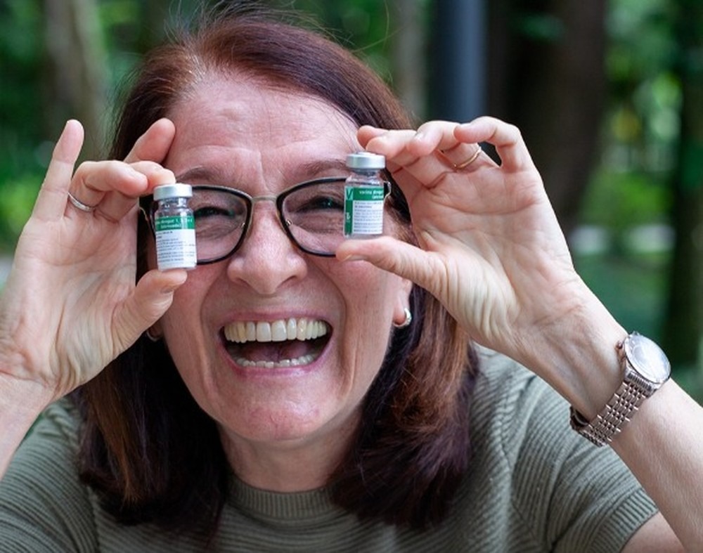 Mulher sorrindo e segurando dois frascos de vacina sobre os olhos.