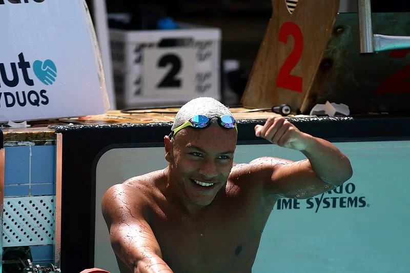 Nadador masculino sorrindo e comemorando na piscina com óculos na cabeça.