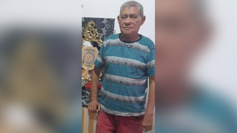 Homem de cabelos grisalhos e camisa listrada posa com emblema da Polícia Civil ao fundo.